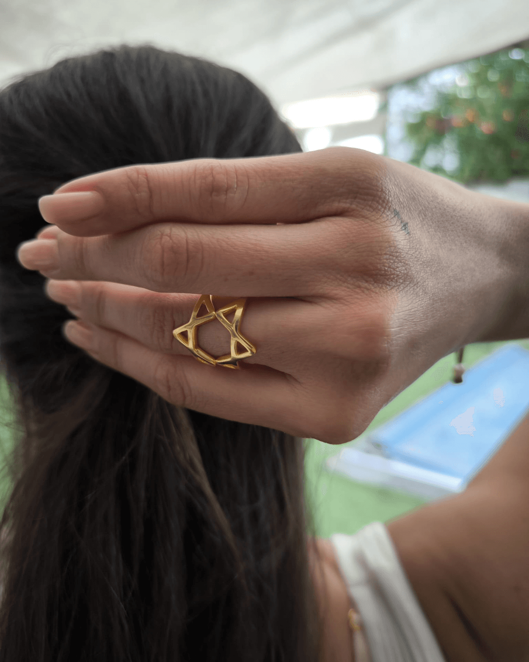 A hand raised to dark hair, wearing the gold vermeil ring: both pieces together on one finger, forming the Star of David.