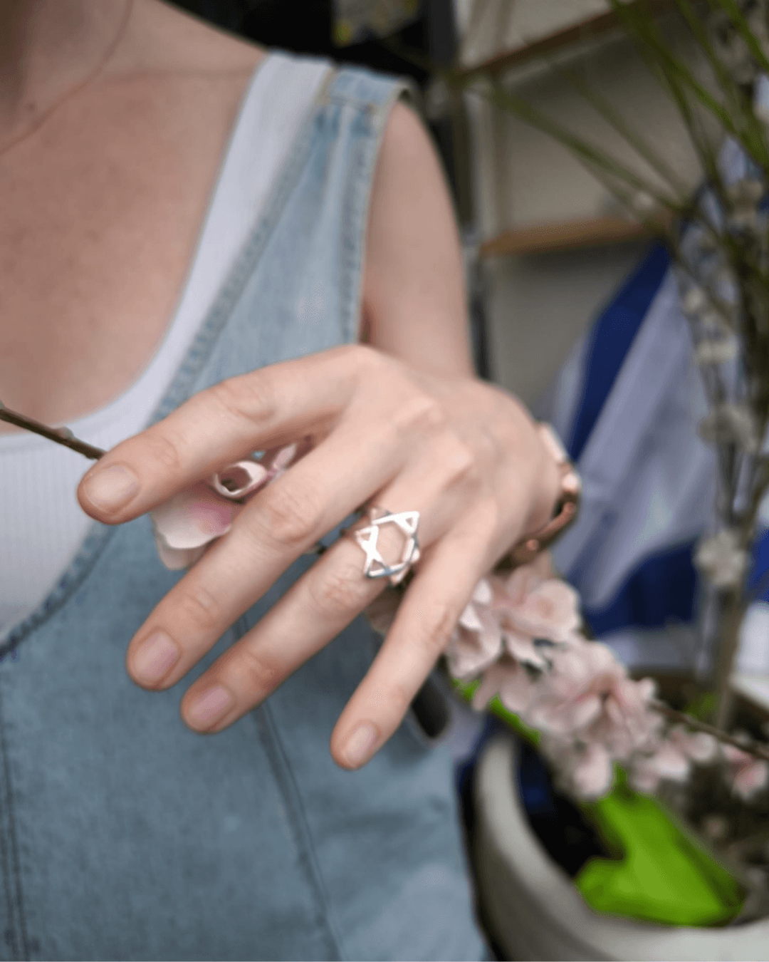 A hand holding a flowering branch, wearing the sterling silver ring: both pieces together on one finger, forming the Star of David.